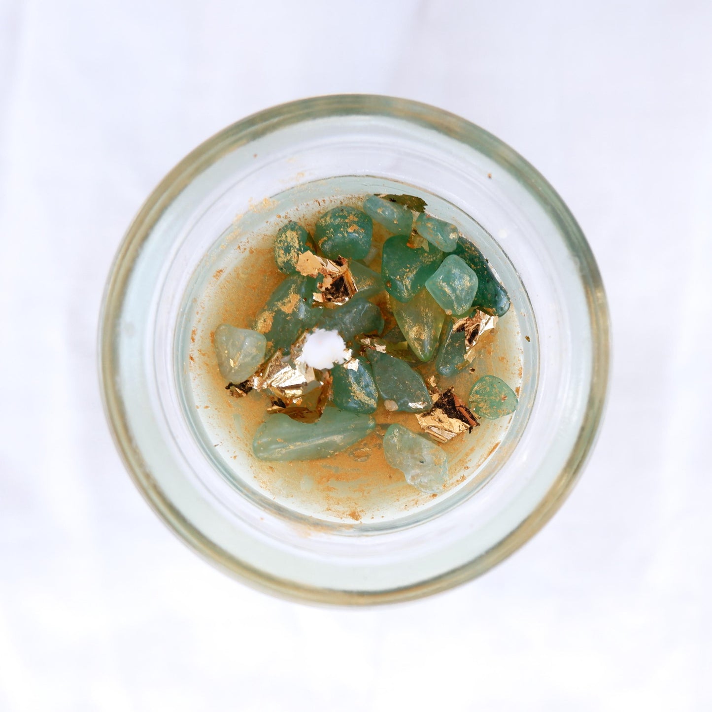 Top view of the Wick & Wish The Lucky one candle in a Glass container with green aventurine crystals and gold elements on a white background