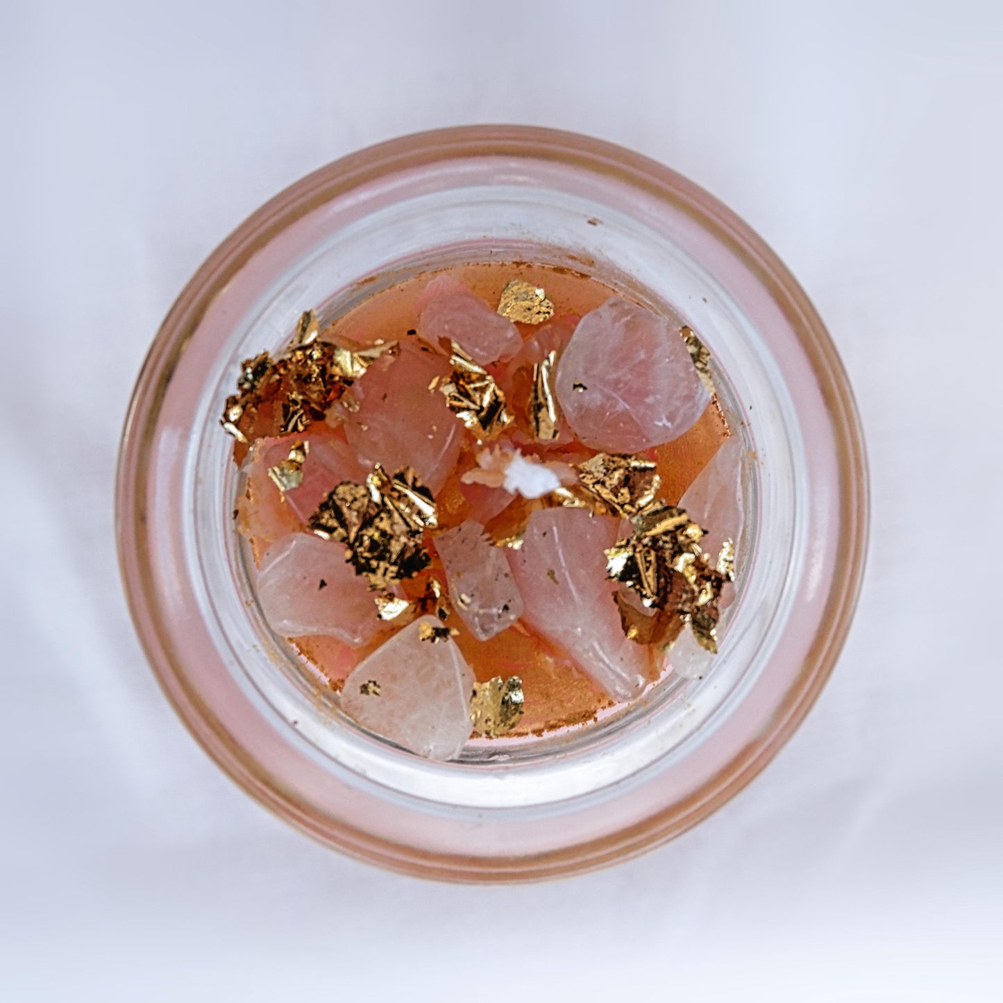 The top view of The Open Heart candle in Glass container with pink rose quartz stones and gold flakes on a white background