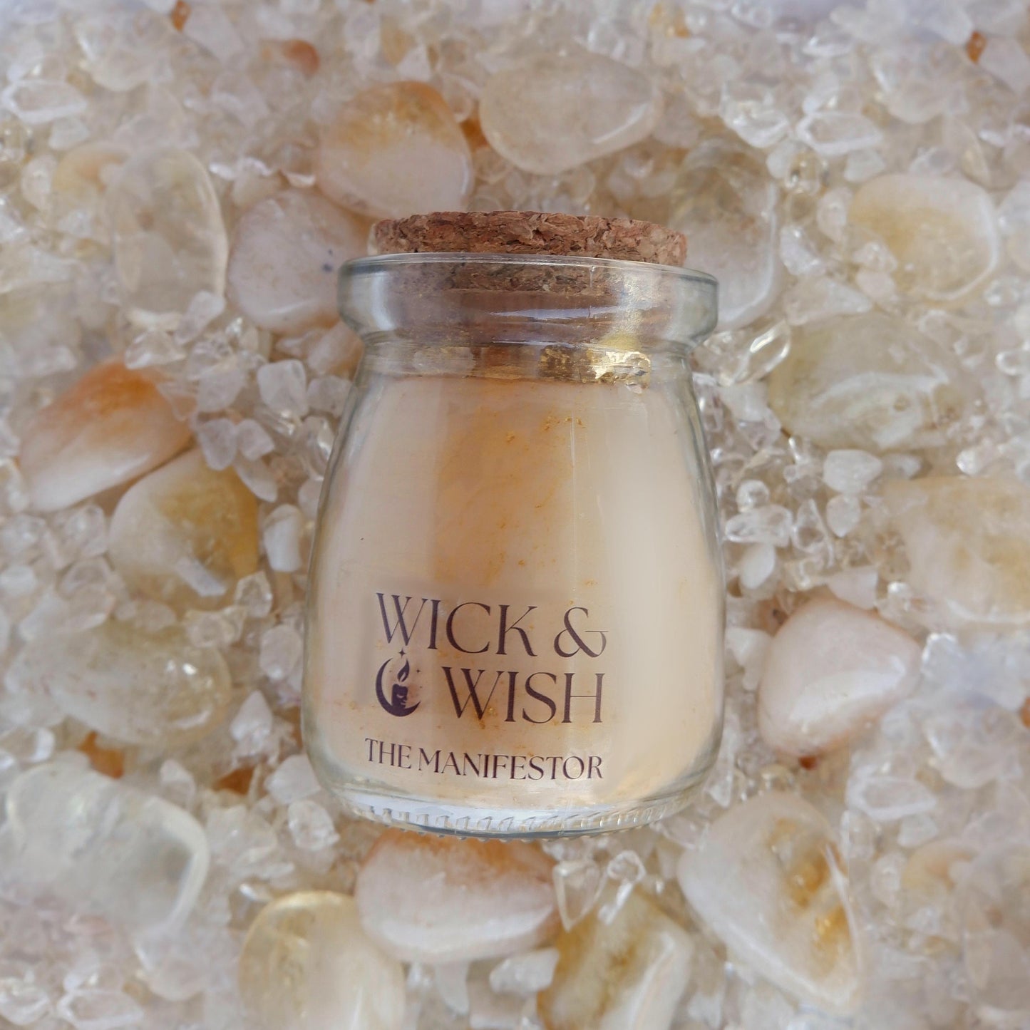 The Manifestor candle labeled 'Wick & Wish' on a bed of citrine stones