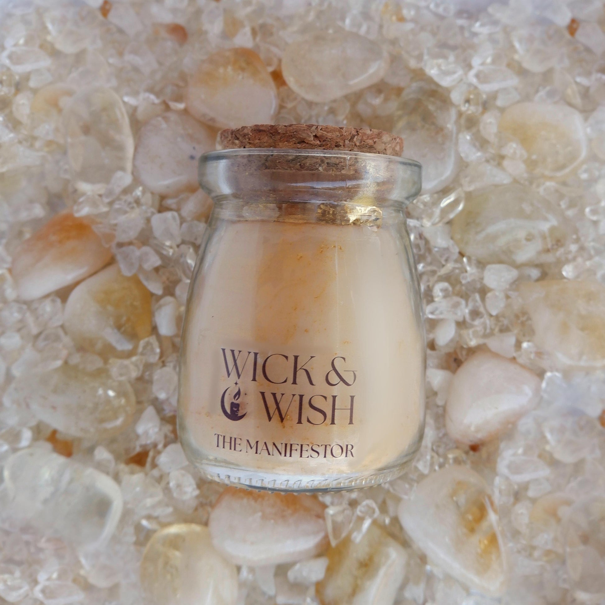 The Manifestor candle labeled 'Wick & Wish' on a bed of citrine stones