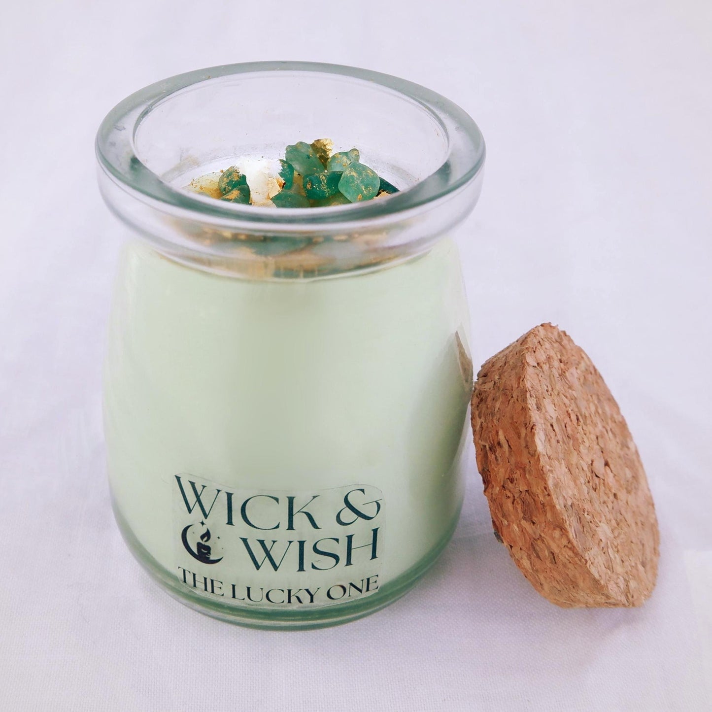 The Lucky One Candle in a glass jar with a cork lid, featuring the brand 'Wick & Wish'.