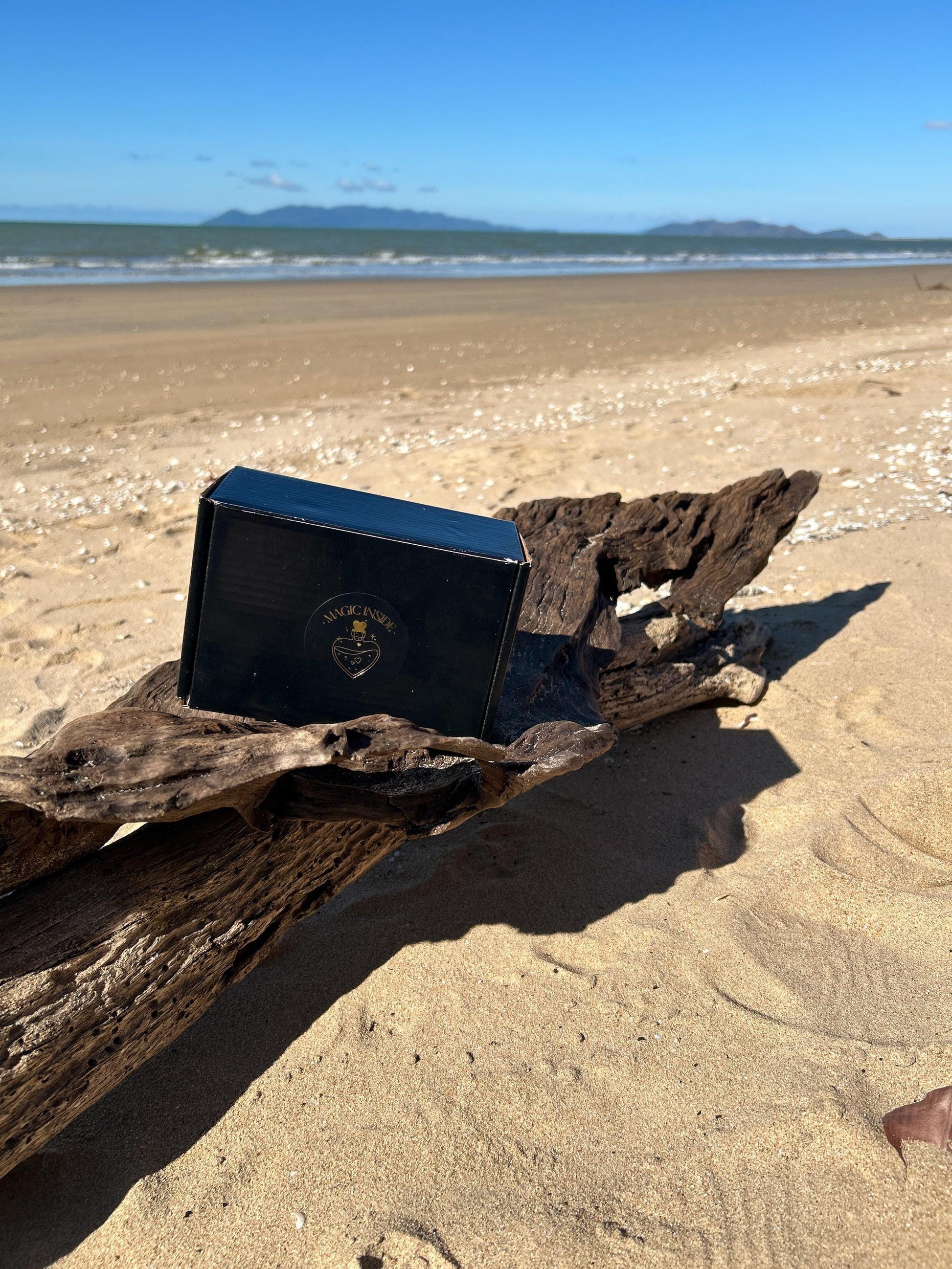 Black packaging with Magic Inside on the top sitting on driftwood on the beach.