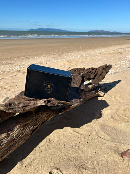 Black packaging with Magic Inside on the top sitting on driftwood on the beach.