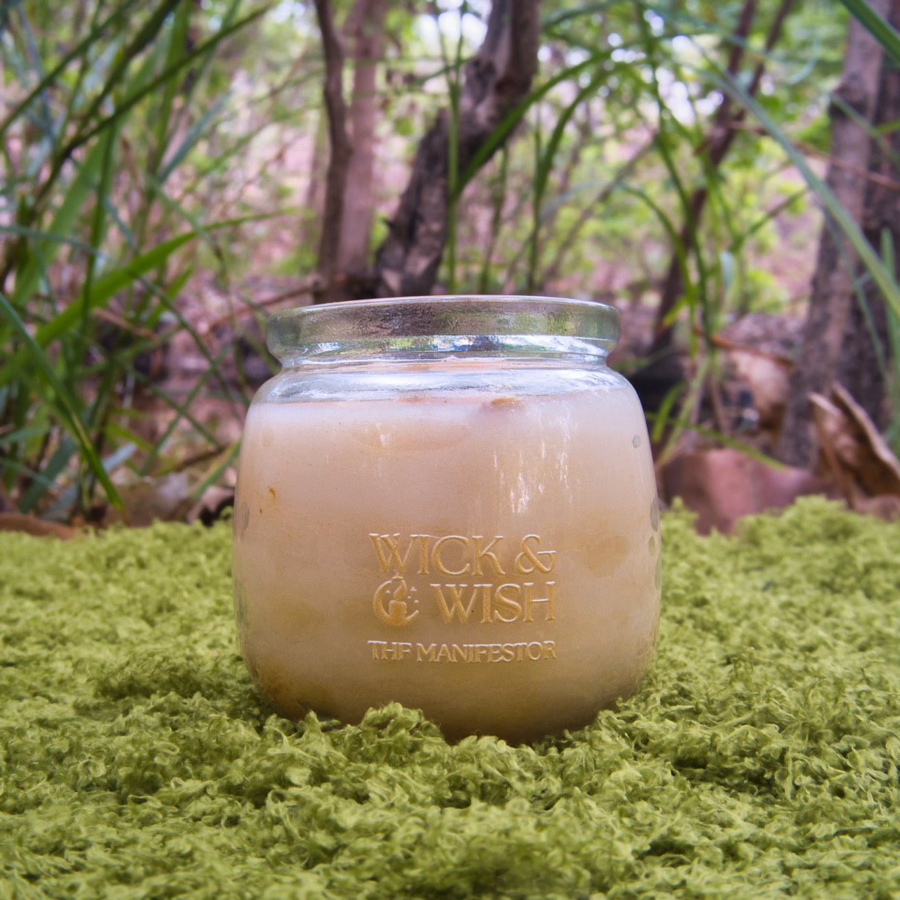 GoldCandle in a jar with 'Wick & Wish The Manifestor' branding on a grassy background