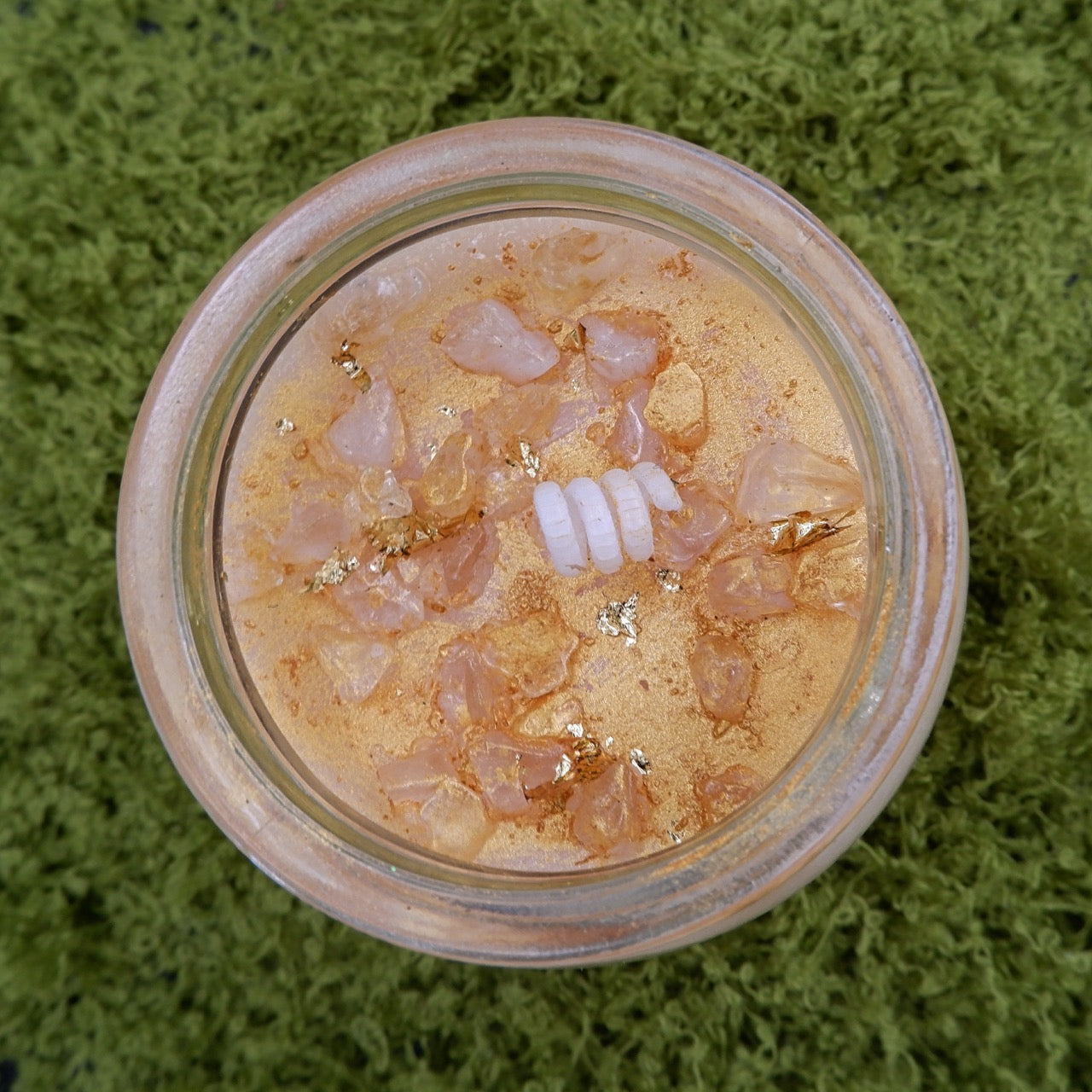 Close-up and top view of Wick & Wish The Manifestor candle with a white twirled wick on a green textured background