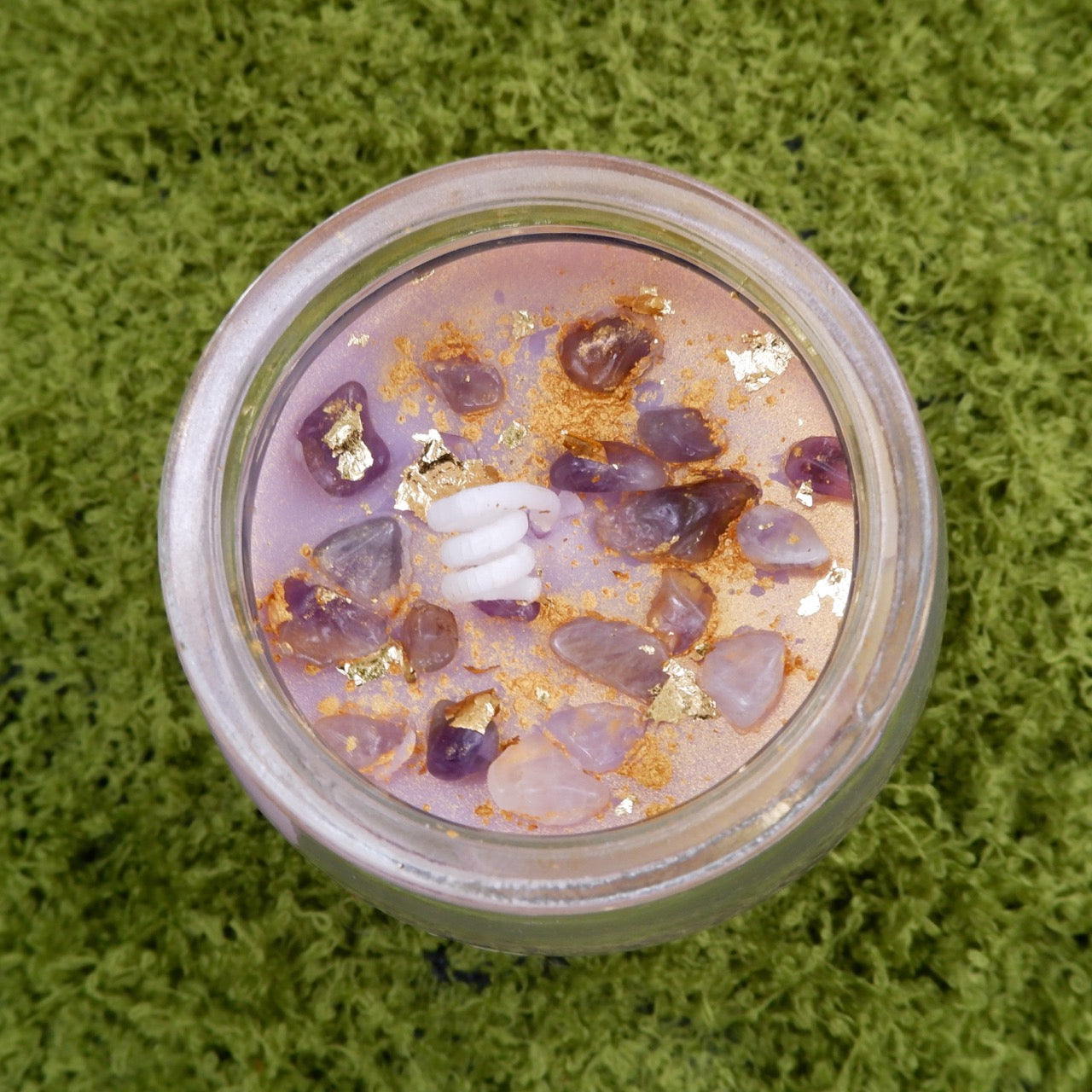 Candle in a jar with a purple, amethyst chips, and gold dusted interior on a green textured background