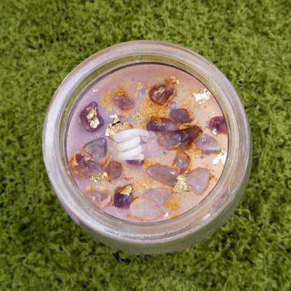 Candle in a jar with a purple, amethyst chips, and gold dusted interior on a green textured background